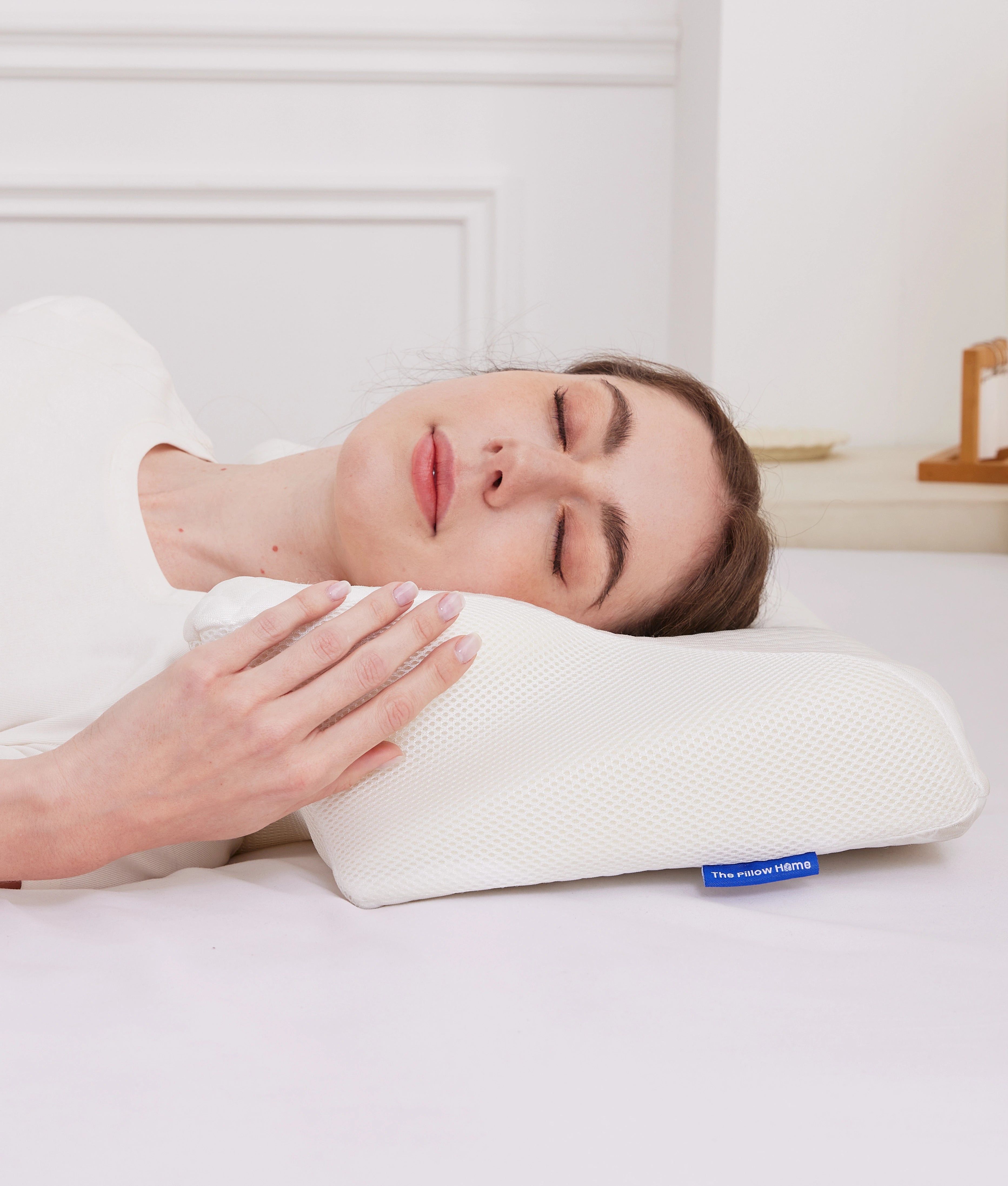 Woman asleep on her back on the CozyRest pillow in its white breathable mesh cover, one hand resting on the pillow