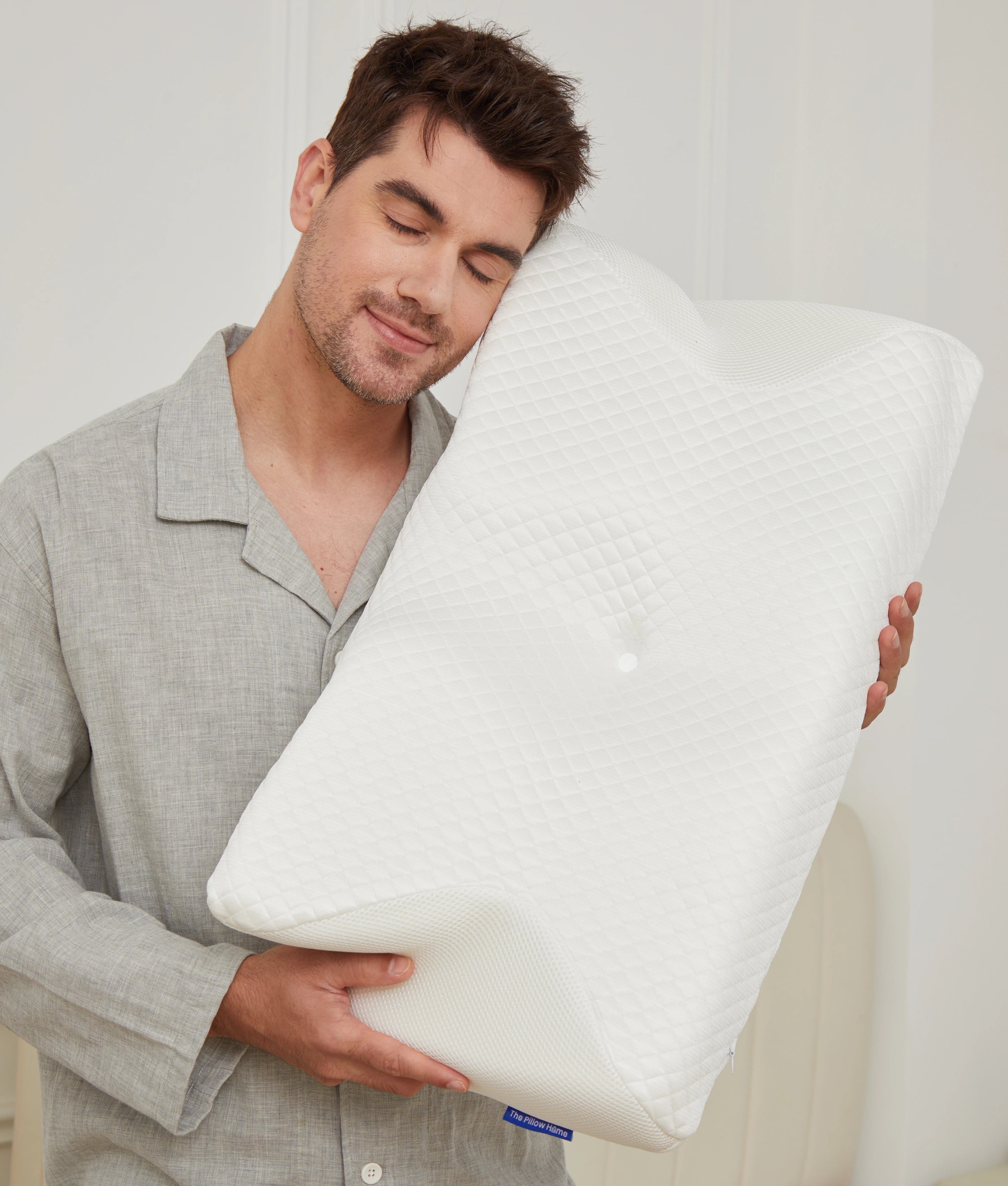 Man in grey linen pajamas hugging the white CozyRest pillow against his cheek with his eyes closed