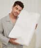 Man in grey linen pajamas hugging the white CozyRest pillow against his cheek with his eyes closed