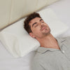 Man in a grey pajama shirt sleeping on his back, his head resting in the center of the white CozyRest pillow against a cream headboard
