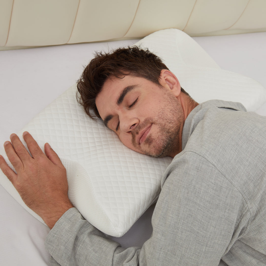 Man in grey pajamas sleeping on his side with his cheek on the white CozyRest pillow and his hand resting on its edge