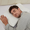 Man in grey pajamas sleeping on his side with his cheek on the white CozyRest pillow and his hand resting on its edge